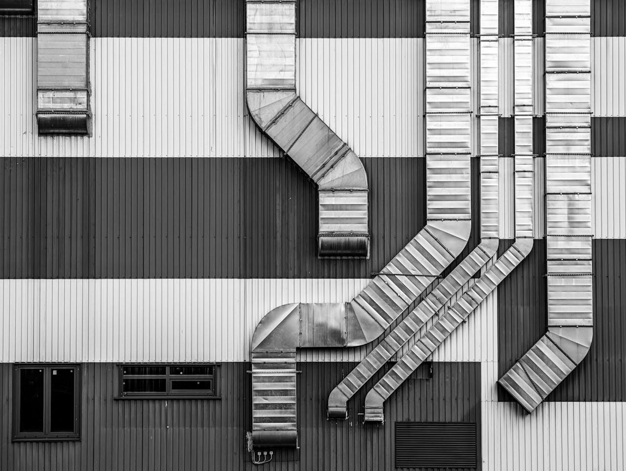 Monochrome image showcasing industrial ductwork and vents on a striped building exterior.
